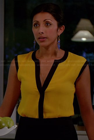Divya’s yellow top with black trim and blue earrings on Royal Pains